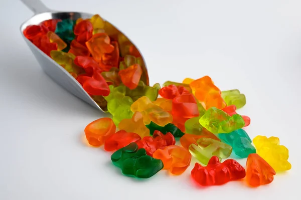 Metal scoop full of colorful gummy candies on white background