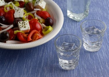 İki bardak ve geleneksel içecek Ouzo veya Rakı ve mavi mat beyaz tabakta geleneksel Yunan salatası şişe 