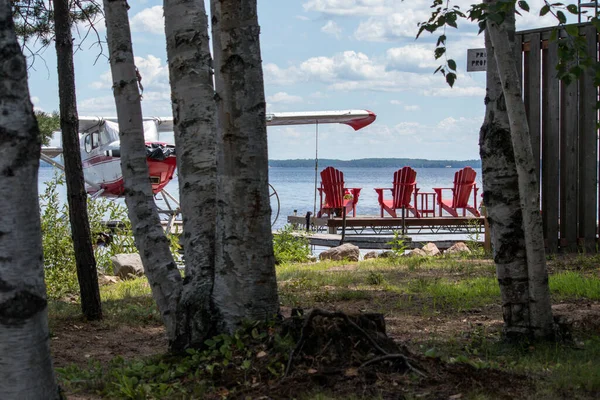 Killaloe, Ontario / Kanada - 24 Temmuz 2020: Rıhtıma bakan üç kırmızı muskoka sandalyesi ve yanında kenetlenen bir uçak.
