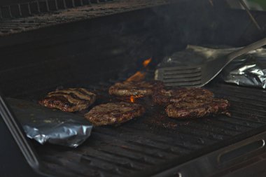 Alüminyum folyoya sarılı hamburgerler ve patatesler barbeküde pişiriliyor. 
