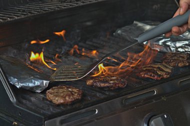Alüminyum folyoya sarılı hamburgerler ve patatesler barbeküde pişiriliyor. 