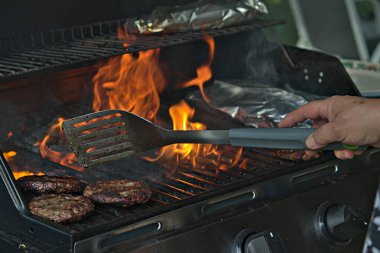 Alüminyum folyoya sarılı hamburgerler ve patatesler barbeküde pişiriliyor. 