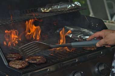 Alüminyum folyoya sarılı hamburgerler ve patatesler barbeküde pişiriliyor. 