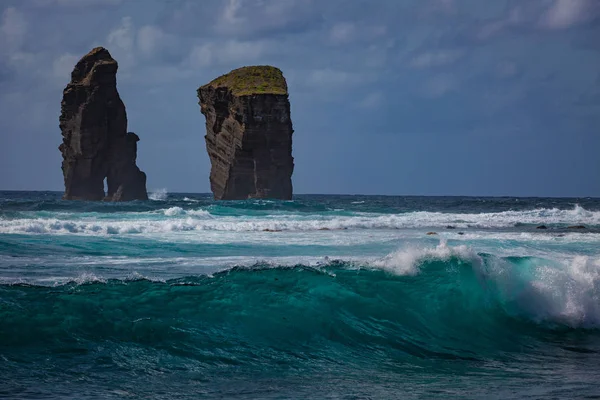 Azores, Atlantic ocean, San Miguel island coast with rough ocean with blue green splashing waves two cliff rocks in water  and cloudy sky on background