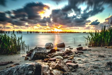 IJsselmeer ve fırtına bulutlu gökyüzü manzarası ile su üzerinde günbatımı. Güneş kirişler mezarlardan parlıyor. sisli su ve dramatik atmosfer ile uzun deklanşör süresi fotoğrafçılığı