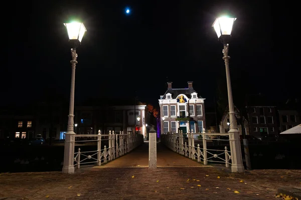 White painted bridge with classic details and traditional street lanterns. Smits work from the time of the industrial revolution with authentic details. View of the town hall and the harbor of the North Dutch city of Harlingen in the province of Frie