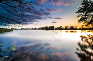 Hollanda, Overijssel 'deki IJssel nehri boyunca suyla dolu bir sel ovasında gün batımından sonra sakin bir akşam sahnesi.