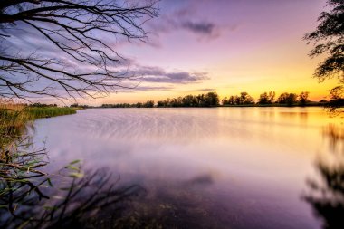Hollanda, Overijssel 'deki IJssel nehri boyunca suyla dolu bir sel ovasında gün batımından sonra sakin bir akşam sahnesi.