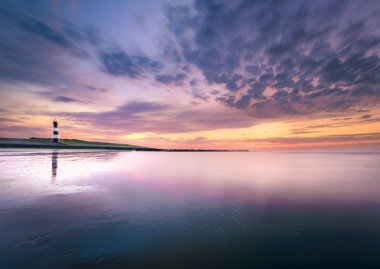 Hollanda kıyıları boyunca atmosferik gün batımı renkli bulutlu gökyüzü ve Hollanda 'nın Breskens kentindeki Zeeuws Vlaanderen köyünün deniz feneri ile Westerschelde' nin zirvesinde. Provinice Zeeland