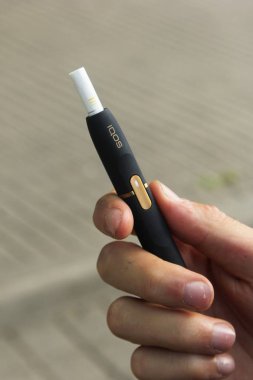 Riga, Letonya, 24 Ocak 2019: IQOS yeni bir ısı-yanmaz tütün ürünü teknolojisi. Sakallı, hibrit sigara içen bir adam. Tütün sistemi IQOS.
