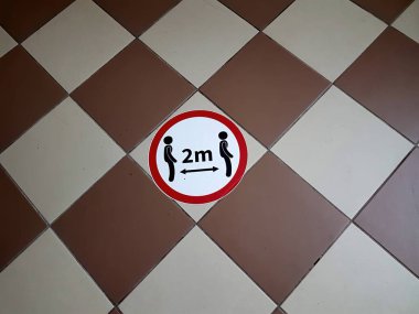 Üzerinde iki kişinin sembolü olan yuvarlak bir tabela ve 2M harfleri fayanslı zeminde 