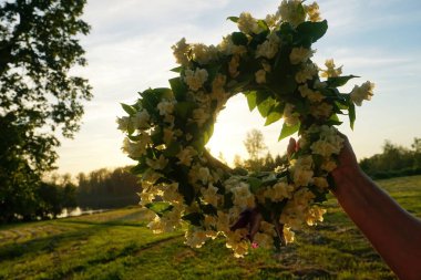 Beyaz yasemin çiçeklerinden oluşan bir çelengi tutan kadın eller akşam güneşinin arka planında. Güzel Yaz ortası Beyaz Çiçek Taç                     