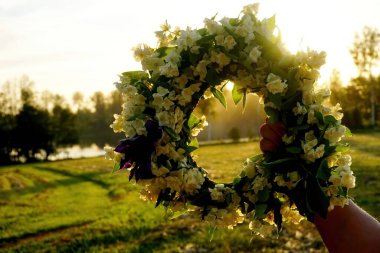 Beyaz yasemin çiçeklerinden oluşan bir çelengi tutan kadın eller akşam güneşinin arka planında. Güzel Yaz ortası Beyaz Çiçek Taç                     