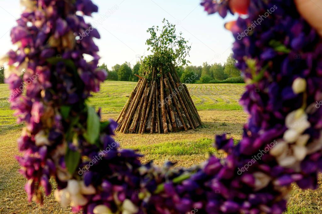        Hands with a wreath of Midsummer purple flowers against the midsummer bonfire                       