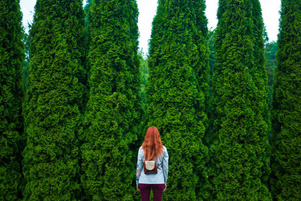 Redhead girl standing in front of green cedars