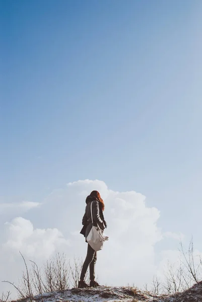 Tall woman standing on blue cloudy winter sky background