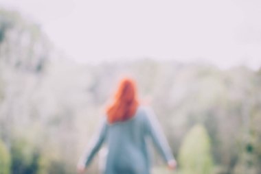 Ufuk arka plan bulanık. Kızıl saçlı kız tepenin önünde dağ orman kenarında duran ve ellerini yükselterek gri bir ceket giyiyor. Konsept (fikir) özgürlük, rüya, sakinlik, meditasyon ve motivasyon.