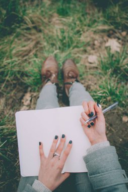 Not defterinde düşünceleri aşağı yazma yeşil bahar çimenlerin üzerinde oturan kızıl saçlı kız. Solgun elleri ve boş kağıt defter. Konsept (fikir) rüya, motivasyon, düşünme, planlama, eğitim.