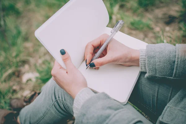 ノートに彼女の考えを書き留めて緑の春の草の上に座っている赤毛の女の子 薄い手 ノートの白紙 やる気 コンセプト 考え方 を計画する勉強 — ストック写真