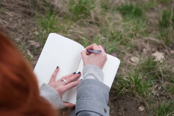 Redhead Dziewczyna Siedzi Trawie Zielonej Wiosny Pisania Notesie Blade Ręce — Zdjęcie stockowe