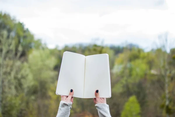 Girl holding a notebook. Pale hands and blank paper of notebook. Concept (idea) of thinking, dreaming, motivation, planning, studying. Background