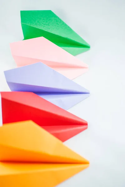 Colorful paper planes. Red paper plane among green, blue, peachy, and yellow ones on a white background, isolated. Concept (idea) of airlines, freedom, leadership, success, and individualism.