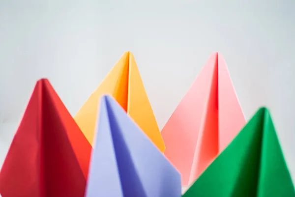 Colorful paper planes. Red paper plane among green, blue, peachy, and yellow ones on a white background, isolated. Concept (idea) of airlines, freedom, leadership, success, and individualism.