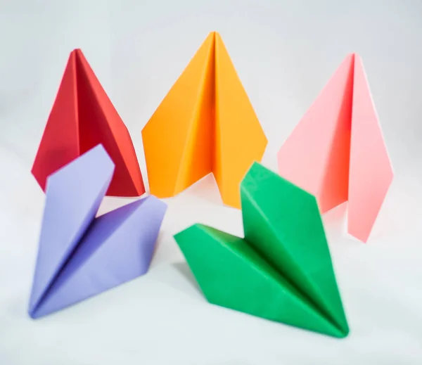 Colorful paper planes. Red paper plane among green, blue, peachy, and yellow ones on a white background, isolated. Concept (idea) of airlines, freedom, leadership, success, and individualism.