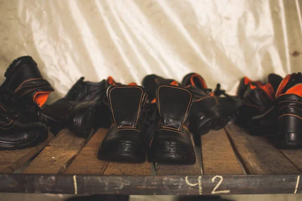 Emergency services work boots. Heavy black leather shoes used in cases of natural disasters, ecological catastrophes, armed conflicts, fires. Boots standing on the wooden shelf in the storage.