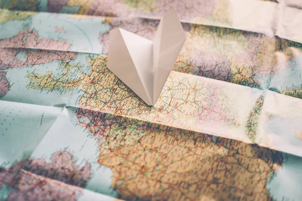 Closeup of a traveler\'s road map in vintage retro colors.  White paper plane flying over Europe