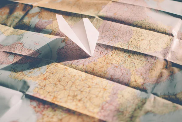 ヴィンテージ レトロな色で旅行者の道路地図のクローズ アップ ヨーロッパ上空を飛ぶ白い紙飛行機 — ストック写真