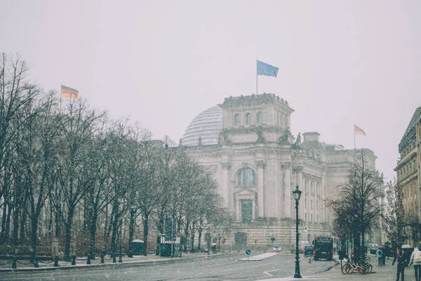 Winter cityscape of Berlin covered with snow. Snowflakes flying against Bundestag. Flags of European Union and Germany seen through snowstorm