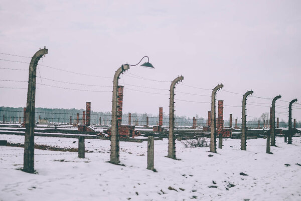 Oswiecim, Poland - February 16, 2018: The electrified barbed wire fence of Auschwitz concentration camp. The remains of the camp on the background