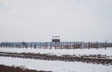 Oswiecim, Poland - February 16, 2018: Railway tracks of Auschwitz concentration camp and a watchtower. clipart