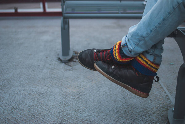 Colorful socks inside brown travel shoes of a man sitting on grey metal bench of public transport boat in Hamburg, Germany