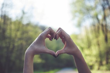 Kız bir kalp yapma şekli jest güneşli yeşil arka plana karşı.