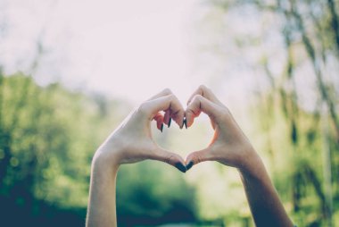 Bir kalp şekli jest güneşli yeşil arka planı gösteren kız.