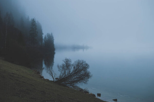 Mysterious mountain lake in early spring morning. Spooky dense fog covering the water.  Sleepy misty landscapes in Alps, Austria.