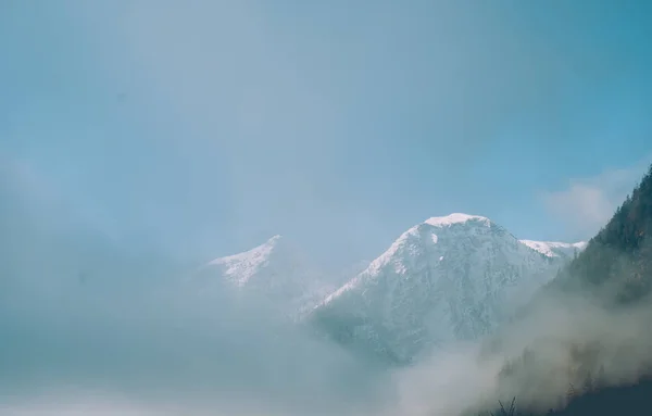 White summit of mountain covered with snow. Dense spring fog in Austrian Alps. Vintage colors