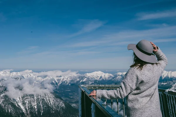 Stylish girl posing against clear sky and snowy mountain peaks in Austrian Alps. Look from behind. Five Fingers, Obertraun