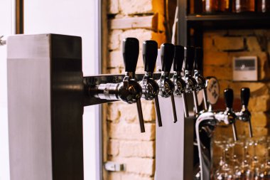 Yakın çekim parlak bira barda güneşli bir öğleden sonra musluklar. Pencereden gelen sarı günlük ışık. Temiz gözlük ve arka plan üzerinde tuğla duvar. Hipsterish iç bar.