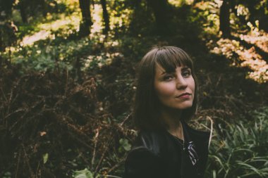 Yakışıklı genç kız ormanda yürüyüş kristal mavi gözleriyle kameraya benziyor. Renkli güneşli yeşil arka plan. Beyaz beyaz modeli