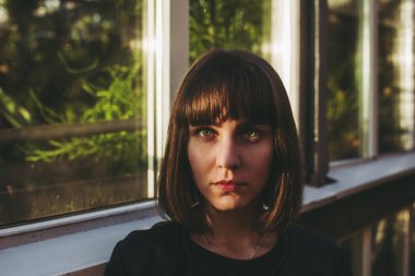 Beyaz beyaz modeli kameraya bakıyor. Sarı güneş ışığı kristal yeşil gözleri yüzünün sağ tarafında üzerinde gösterilir. Sera yeşil bitkiler ile arka plan üzerinde bina. Sonbahar öğleden sonra.