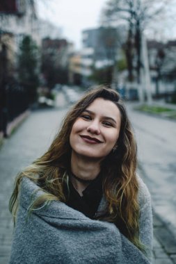 Gülümseyen genç kız kaldırımda ayakta. Sonbahar yağmur sonra mavi ıslak asfalt. Erken akşam.