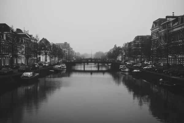 Charmant stadsgezicht van de oude Nederlandse stad Haarlem. Stenen brug die twee oevers van de rivier de Spaarne verbindt. Prachtig perspectief. Mistig en bewolkt vroeg voorjaar weer. Zwart-wit — Stockfoto