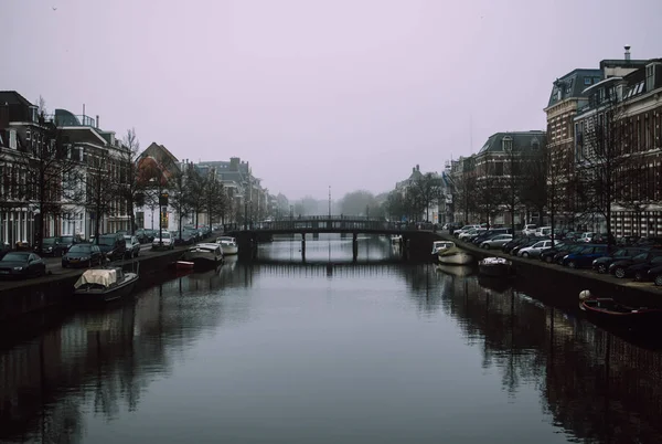 Uroczy pejzaż starego holenderskiego miasta Haarlem. Kamienny most łączący dwa brzegi rzeki Spaarne. Spokojna niebieska woda i czarne cienie. Piękna perspektywa. Mglisty i pochmurno wczesna Pogoda wiosenna. — Zdjęcie stockowe
