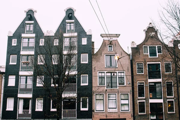 Casas holandesas de tijolos tradicionais em Amsterdã, Holanda. Paredes de fachada preta e pastel estreitas com janelas altas contra o céu cinzento nublado . — Fotografia de Stock