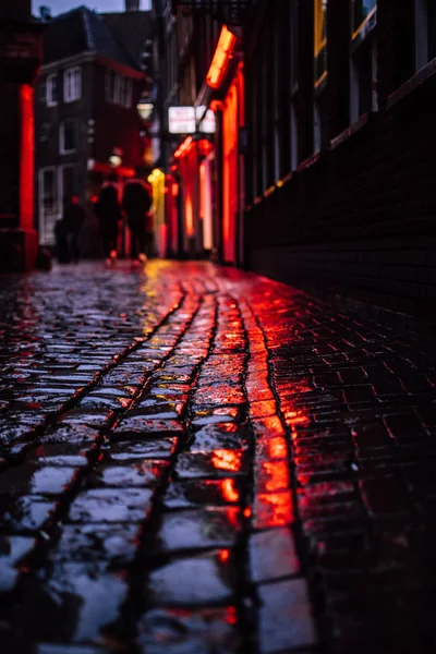 Rode LIGTHS van een beroemd rood licht Japans in Amsterdam, Nederland. Reflectie van neon verlichting van etalage ramen over natte stoep in een donkere schaduwrijke doorgang. Europese hoofdstad van gelegaliseerde prostitutie en marihuana. — Stockfoto