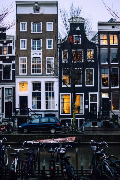 Traditional bricked Dutch houses in Amsterdam, Netherlands. Cars and bicycles in front of the front walls. Window lights reflected in a canal water