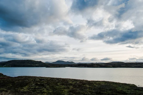 Green mountains covering the banks of the lake in Iceland. Dreamy lancscapes beneath the blue clouldy sky. Stock Picture